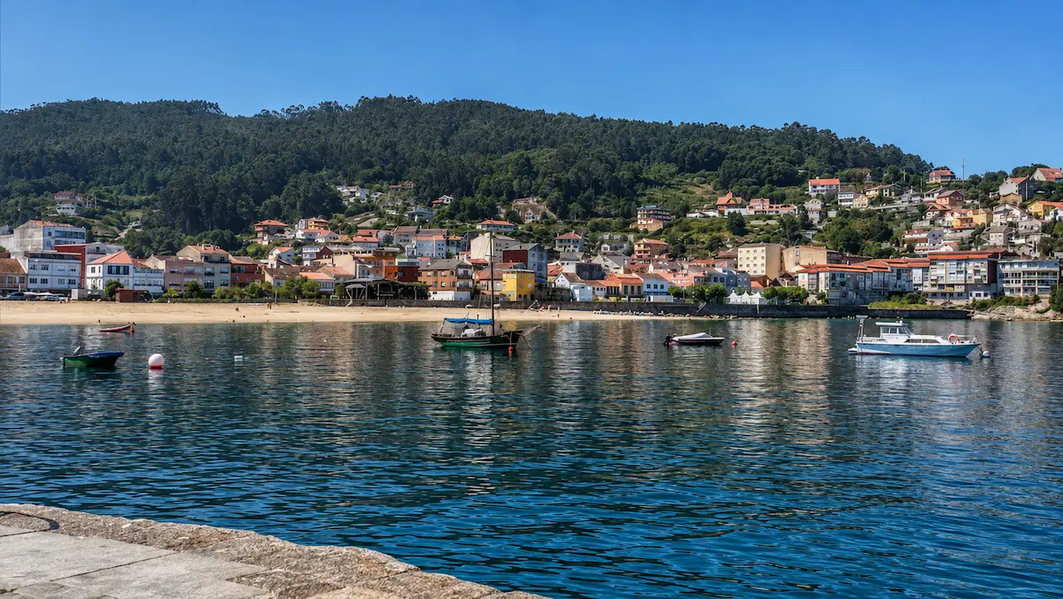 Vista de Bueu desde la ría, con la playa, embarcaciones, casas y monte al fondo.