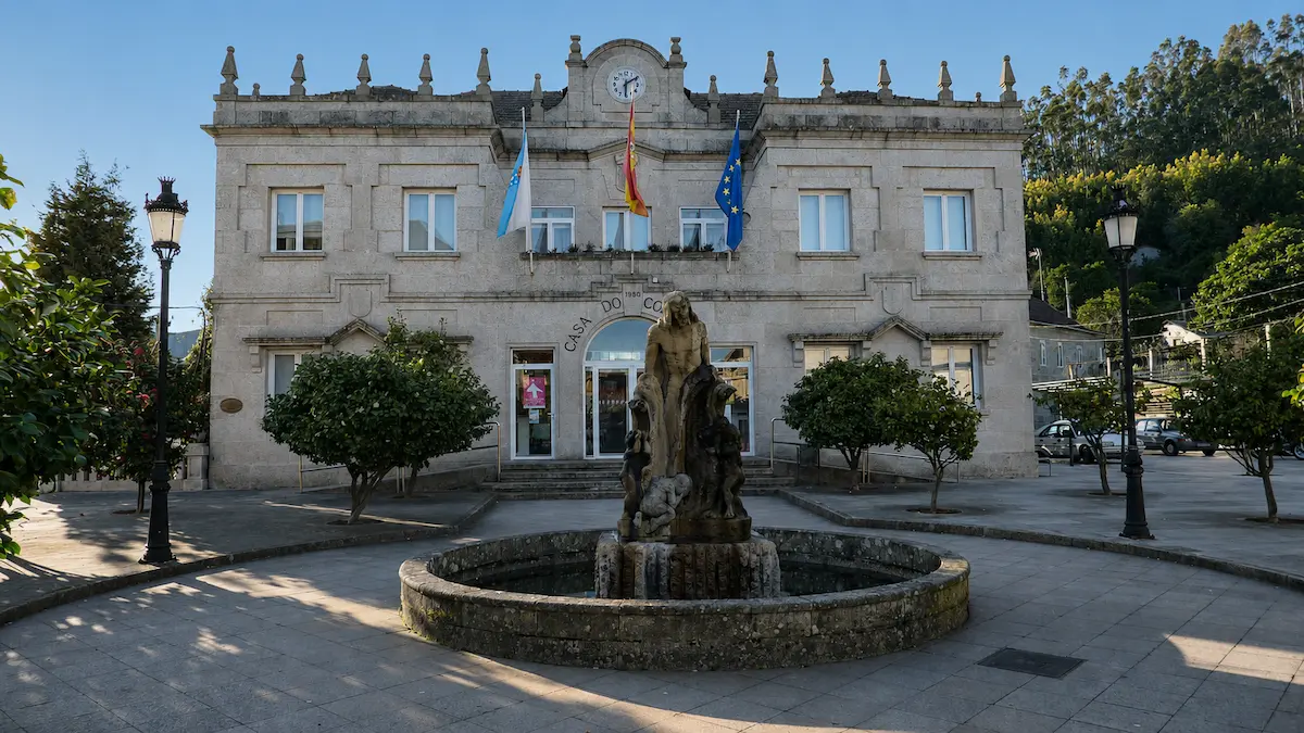 Casa do Concello de As Neves con reloj, banderas y fuente escultórica en la plaza del municipio.
