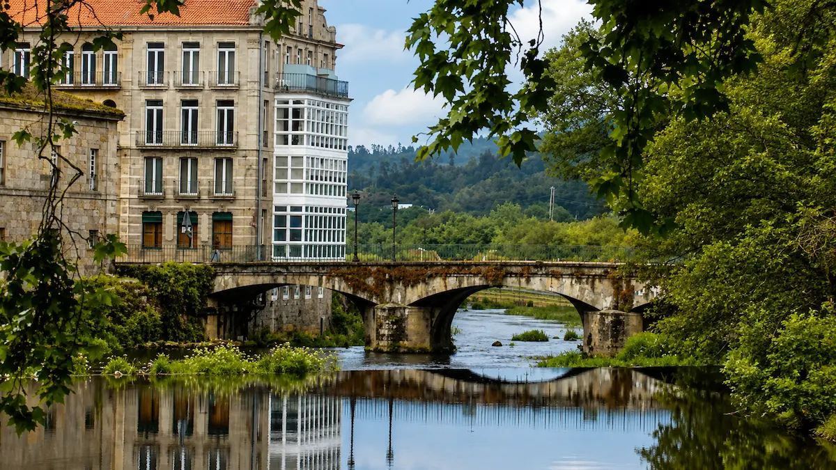 Puente histórico sobre el río Umia en Caldas de Reis, junto a un edificio tradicional y un paisaje verde.