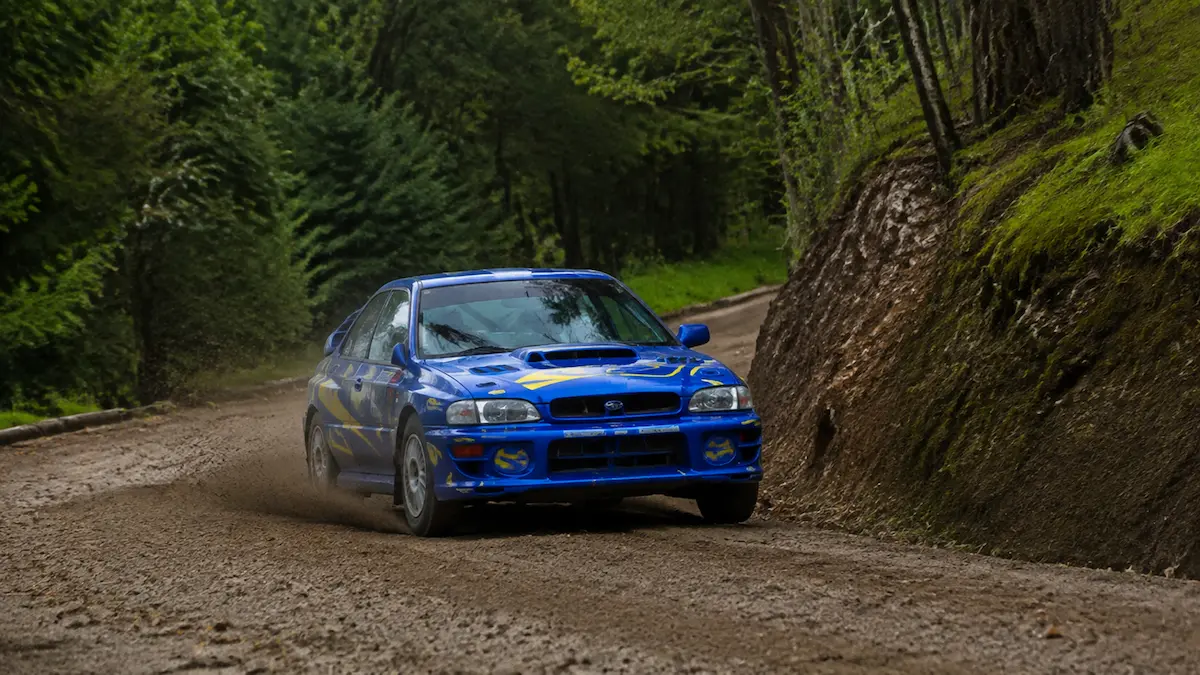 Coche de rally azul y amarillo disputando un tramo de tierra entre los bosques de Cuntis