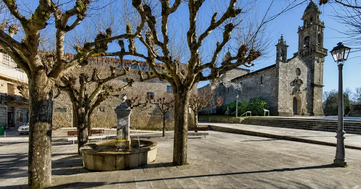 Praza de Cuntis con fonte, árbores e igrexa de pedra ao fondo