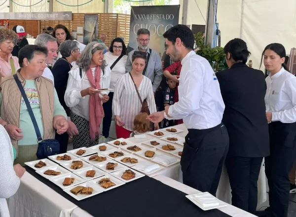 Personas disfrutando de una degustación de empanada de choco en la XXXVII Festa do Choco de Redondela, con un chef sirviendo las porciones en un stand gastronómico.