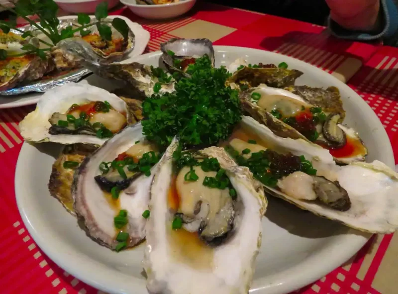 Plato de ostras frescas servidas con salsa y cebollino en un ambiente gastronómico, representando la Festa da Ostra de Arcade 2025 en Soutomaior