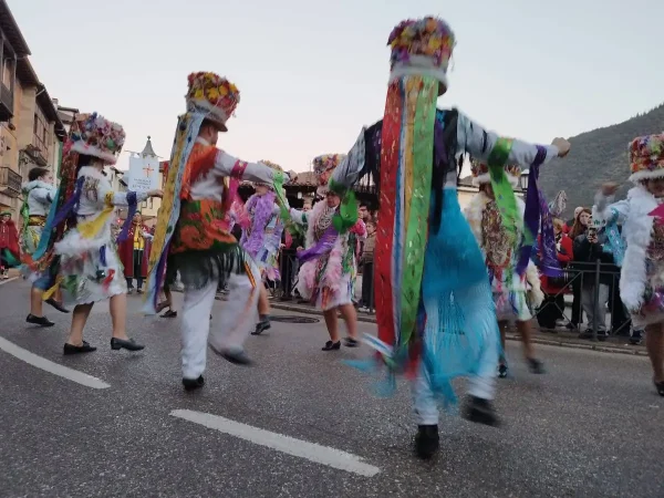 Madamas y Galáns con trajes tradicionales coloridos bailando en las calles de Vilaboa durante el Entroido de Cobres, rodeados de espectadores y ambiente festivo.