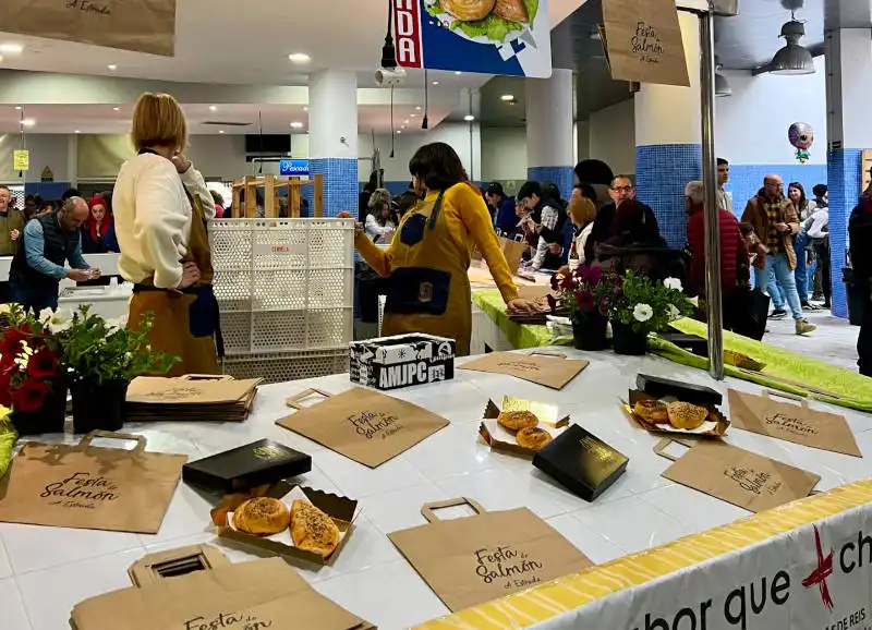 Puesto de degustación con productos de salmón en la Festa do Salmón de A Estrada, con asistentes y organizadores en el evento.
