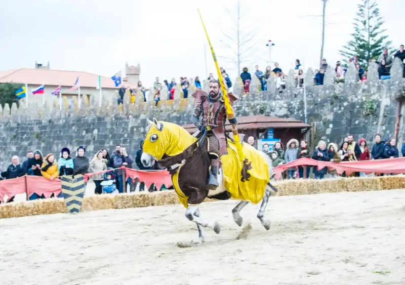 Caballero participando en un torneo medieval durante la Festa da Arribada de Baiona, con espectadores y ambiente medieval.